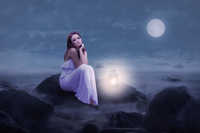 黑夜里一个女人拿着一盏灯坐在海边的石头上