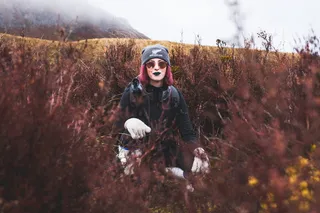 紫色头发的女人蹲在灌木丛中间的照片