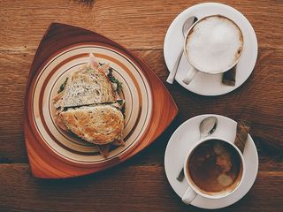 火腿三明治放在盘子里，靠近卡布奇诺，放在杯子和咖啡上