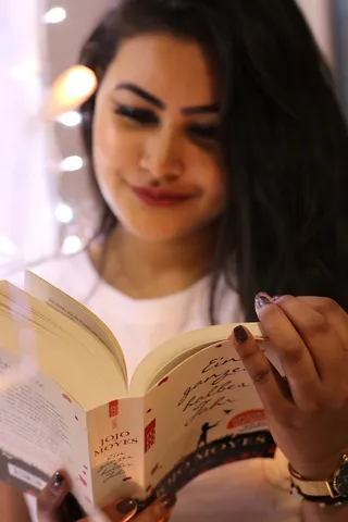 穿着白色圆领衬衫拿着Jojo Moyes书的女人