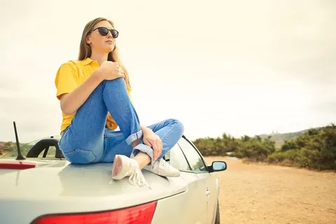 坐在敞篷银色轿车上的年轻女子,身穿半袖黄色衬衫和牛仔牛仔裤,戴着黑色太阳镜 坐在敞篷银色轿车上的年轻女子,身穿半袖黄色衬衫和牛仔牛仔裤,戴着黑色太阳镜