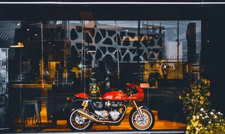 玻璃墙附近带金色头盔的红色标准摩托车