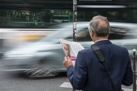 在水泥路面上,一名身穿蓝色西装外套的男子在车辆前方拿着报纸 在水泥路面上,一名身穿蓝色西装外套的男子在车辆前方拿着报纸