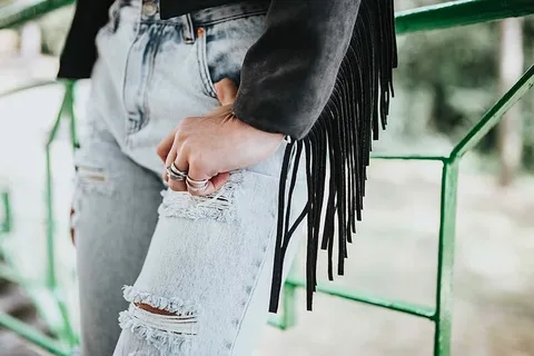 穿着黑色夹克和绿色扶手撕破牛仔裤的金发女人