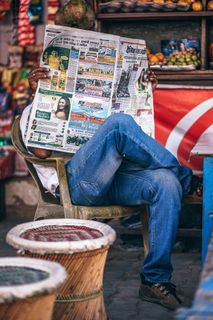 坐在塑料扶手椅上看报纸的男子