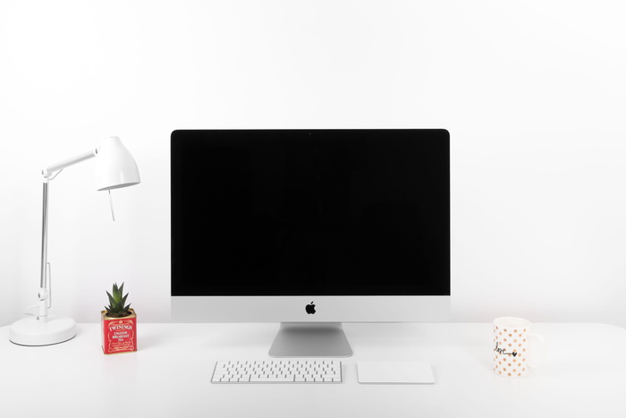 银色iMac、Apple无线键盘和靠近台灯的Apple Magic触控板