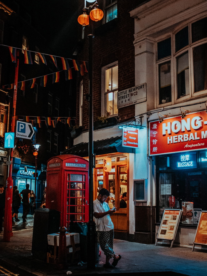 身穿白色衬衫的男子站在棕色和白色水泥大楼前的红色电话亭上