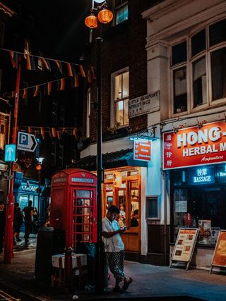 身穿白色衬衫的男子站在棕色和白色水泥大楼前的红色电话亭上