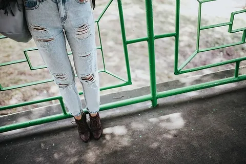 穿着黑色夹克和绿色扶手撕破牛仔裤的金发女人