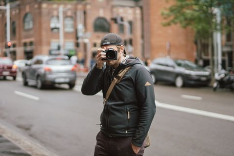 一名男子身穿黑色连帽衫，手持相机拍照