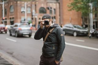 一名男子身穿黑色连帽衫，手持相机拍照