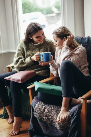 两个女人坐在椅子上拿着杯子，一边笑着聊天