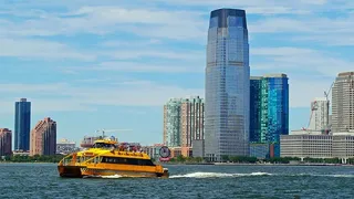 一辆黄色的纽约水上出租车游轮经过哈德逊河上的杰斯利市海滨，驶向纽约港，进行观光游轮。