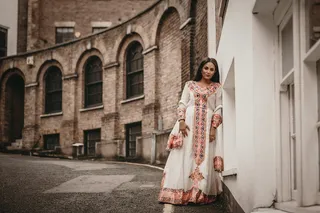 身穿白色和棕色长袖连衣裙的妇女站在白色墙壁附近