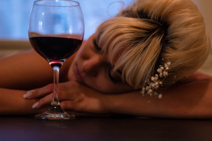 戴着白色花朵口音头饰的女人把头靠在半满的酒杯旁的桌子上