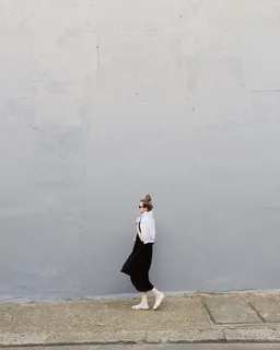 穿着黑色长裙和白色平底鞋的女人站在灰色的墙上
