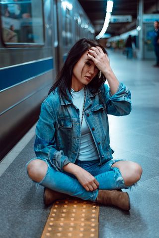 坐在子弹头列车旁的一位身穿牛仔牛仔裤和夹克的女士