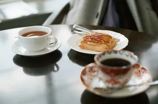 面包放在陶瓷盘上，靠近装满咖啡的白色陶瓷茶杯