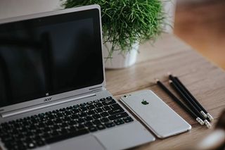 银色宏碁笔记本电脑放在一张木桌子上，上面有一株绿色植物、铅笔和一部苹果iPhone