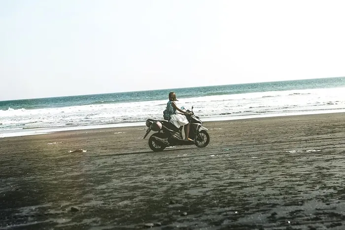 在海滩上骑着黑色和灰色摩托车的女人
