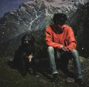 坐在岩石上一条狗旁边的男人