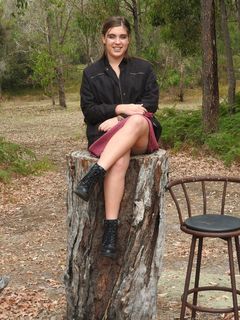 一名身穿黑色夹克的女子坐在酒吧凳子旁的圆木上