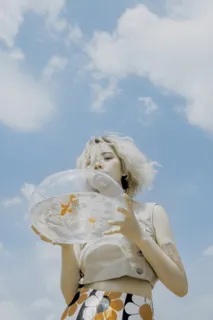 在蓝天白云下,一个女人手里拿着一个装着活鱼的圆形透明玻璃鱼缸 在蓝天白云下,一个女人手里拿着一个装着活鱼的圆形透明玻璃鱼缸
