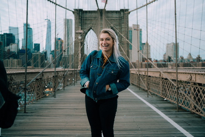布鲁克林大桥站着一位微笑的女士，身穿蓝色牛仔纽扣夹克