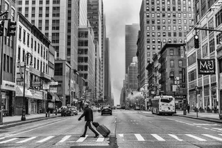 男子拉着行李，走在车辆和建筑物附近的人行道上