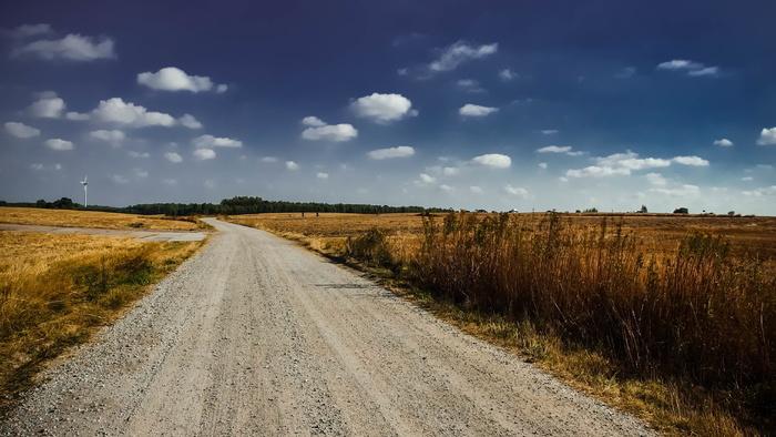 灰色的道路在白色多云的天空下的棕色草地之间