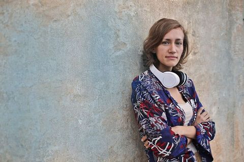 一位身穿五颜六色连衣裙的金发女郎靠墙站着，脖子上戴着耳机