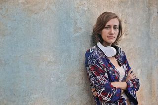 一位身穿五颜六色连衣裙的金发女郎靠墙站着，脖子上戴着耳机