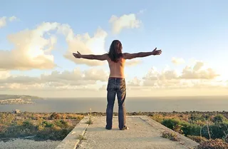 一名身穿牛仔服的男子站在海边，双臂紧握