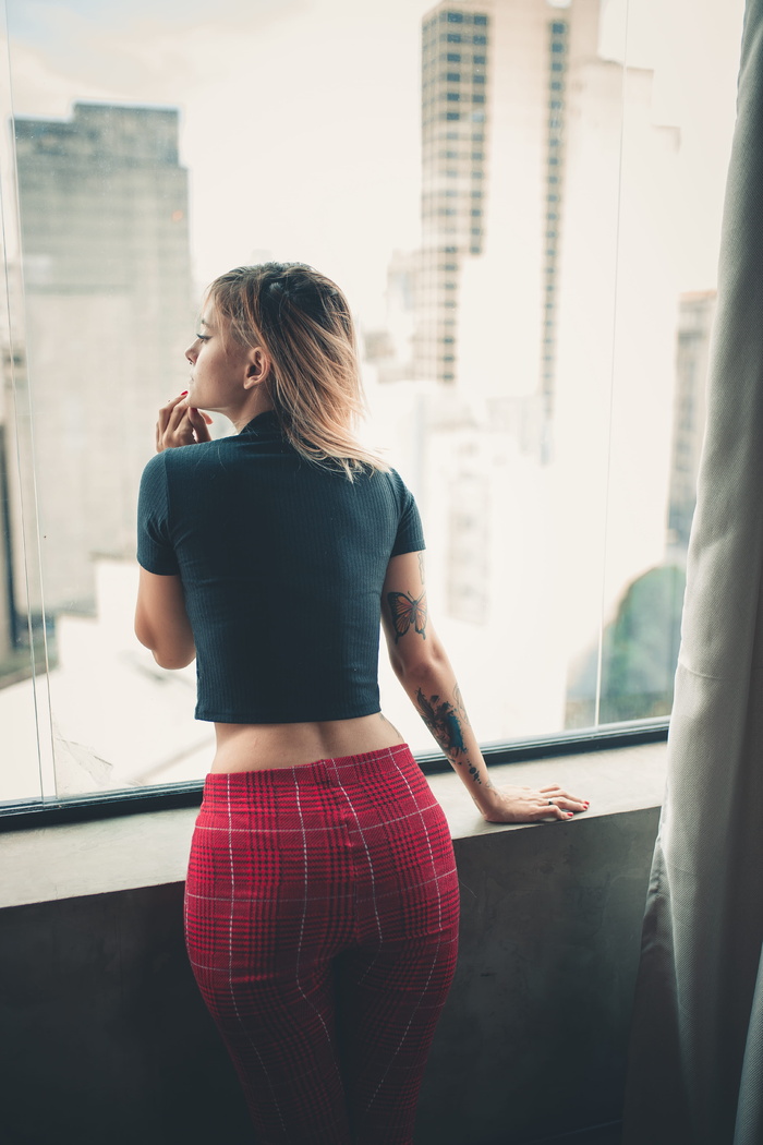 身穿黑色上衣的女子站在窗户旁向外看的后视图照片