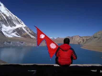 坐在尼泊尔Tilicho湖岸的男子举着国旗。 坐在尼泊尔Tilicho湖岸的男子举着国旗。