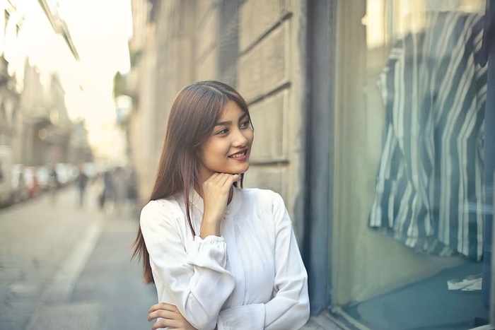 年轻的亚洲女人穿着白衬衫，手放在下巴上在街上逛街