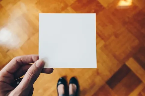 在棕色木地板上拿着白纸的人