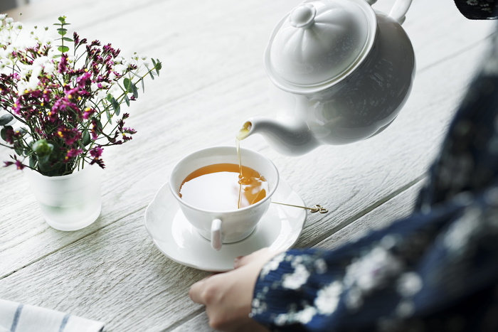 拿着白色陶瓷茶壶在杯子里倒茶的人
