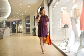 一位身穿紫红色连衣裙、拎着购物袋的金发女郎在商店的橱窗里看