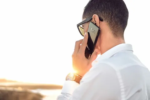一名手持智能手机的男子站在平静的水面前 一名手持智能手机的男子站在平静的水面前