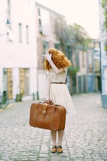 一名身穿白色短袖连衣裙的女子手持棕色皮箱