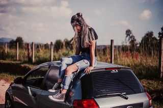 一名身穿黑色衬衫和蓝色牛仔服的女子坐在车顶上