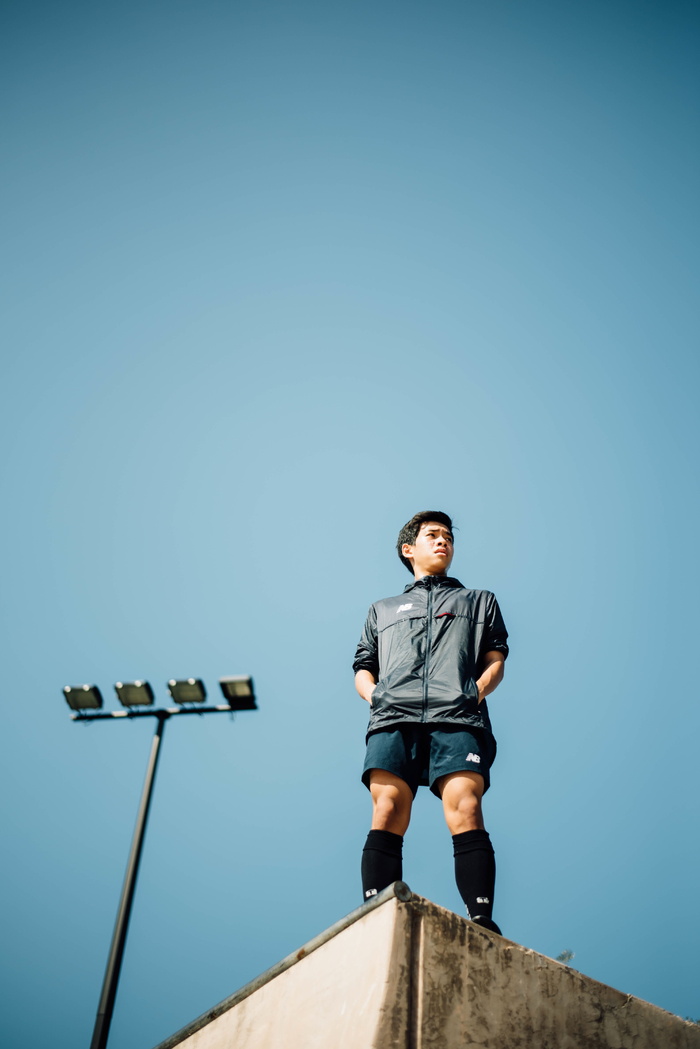 白天，身穿黑色拉链衬衫和蓝色衬衫的男子站在晴朗的蓝天下的楼顶上