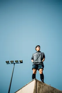 白天，身穿黑色拉链衬衫和蓝色衬衫的男子站在晴朗的蓝天下的楼顶上