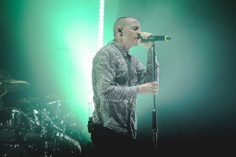 男子身穿灰色纽扣衬衫，手持黑色无绳麦克风，带支架