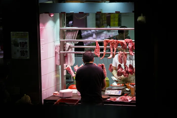 一名男子站在摊位前，手里拿着挂着的肉