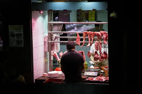 一名男子站在摊位前,手里拿着挂着的肉 一名男子站在摊位前,手里拿着挂着的肉