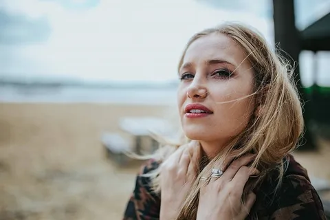 美丽的金发女人在海滩边的树桩上拿着一罐可乐放松