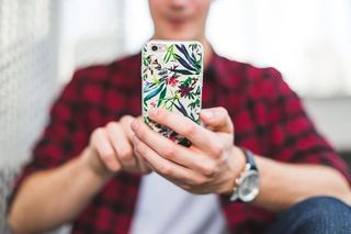 手持五彩花卉Iphone手机壳的人