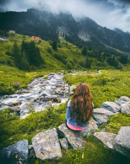 穿着牛仔夹克的女人坐在岩石上面对着山